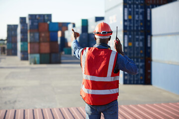 back view African factory worker or engineer using walkie talkie and showing stop gesture to crane car in containers warehouse storage