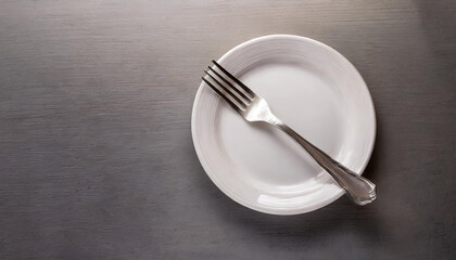 Fork on empty white plate, gray table. Flat lay