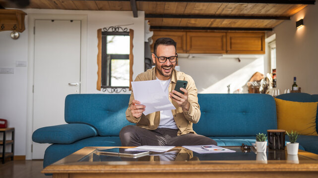 one adult man sit at home make a call while hold paper documents