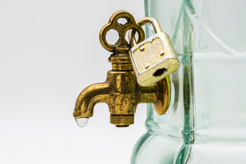 Detalle de un grifo de bronce con una gota de agua, cerrado con un candado, aislado en blanco	