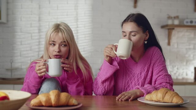 A young lesbians couple spending time together at home. Holiday with girlfriend. Cute couple lesbians drink coffee with french croissant. Mutual love relationships. Two girls transgenders having a