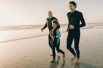 Family in wetsuits running on beach at sunset