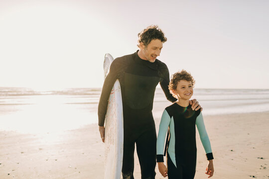 Father and son with surfboard on the beach at sunset