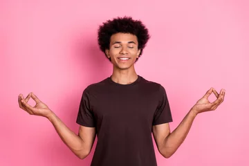 Poster Im Rahmen Portrait of young relaxed young man funny curly hair meditation in lotus pose close eyes and chill isolated on pink color background © deagreez