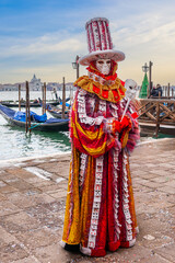 A person dressed for carnival in front of the gondolas and the Venetian lagoon in Veneto, Italy - 753104503