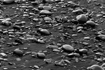 Wet stones, sand and pebbles of black lava with shiny surface in the high tide edge of a beach...