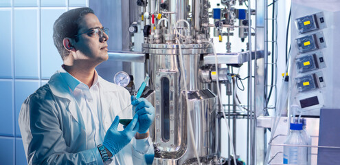 Scientist studying biotechnology. Man stands near bioreactor. Biologist in white coat. Man...