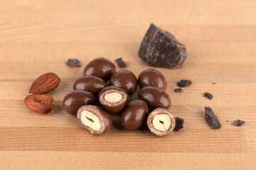 Chunks of dark chocolate and dark chocolate covered nuts on a wooden surface.