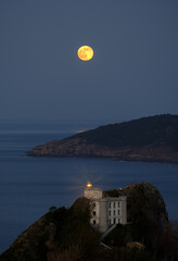 Moon over the silver lighthouse. Full moon and silver lighthouse from Mount Ulia, Euskadi.