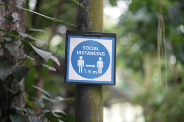 Fototapeta premium A blue social distancing sign displayed on a moss-covered pole in a lush green environment, emphasizing the importance of maintaining a 1.5-meter distance for public health and safety.