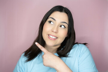 Close-up image of an attractive young woman with long hair and a playful look, making an amused expression, smiling and pointing with her hands.