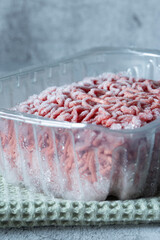 Frozen beef steak mince in a plastic container defrosting. On a green tea towel.