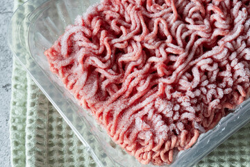 Frozen beef steak mince in a plastic container defrosting. On a green tea towel.