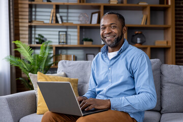 Cheerful man relaxed on sofa with laptop, displaying comfort and productivity in a modern living space.