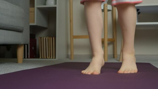 Child jumping barefoot on yoga mat, feet close-up. Childrens sports at home