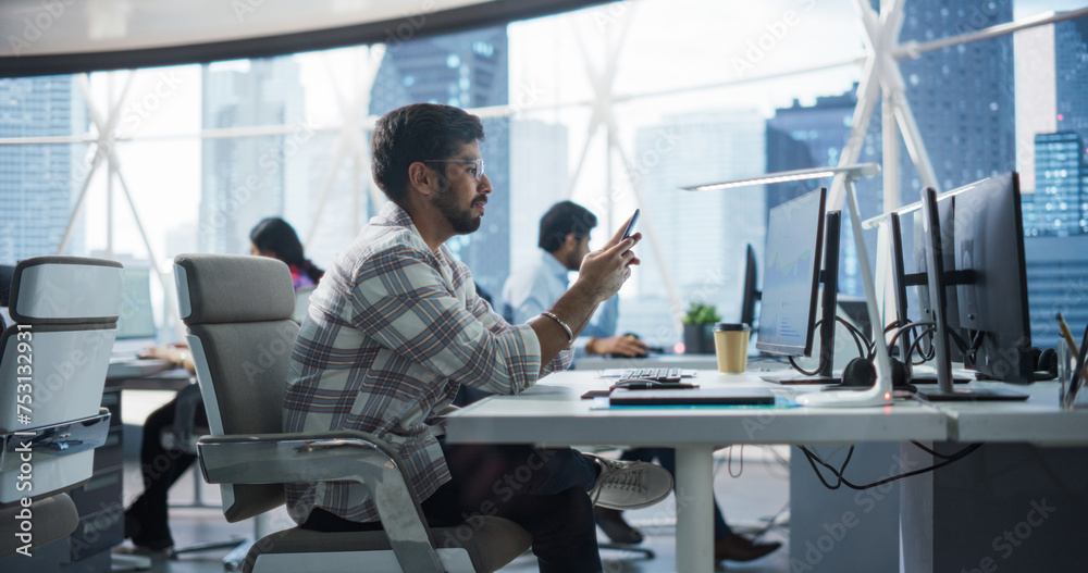 Fototapete portrait of a handsome indian manager using smartphone while sitting behind a desk in a corporate of