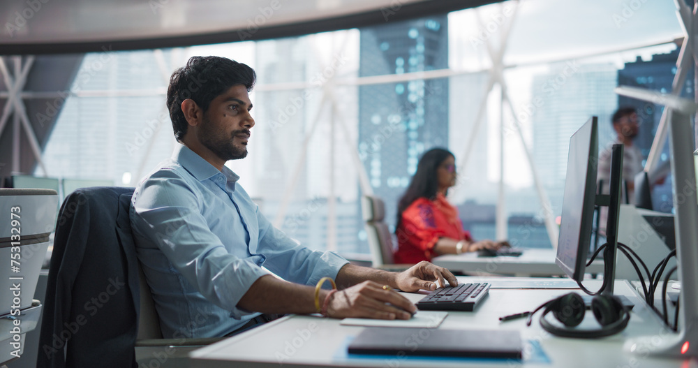 Poster Portrait of an Indian Businessman Working on a Desktop Computer in a Fintech Startup Company. South Asian Financial Analyst Conducts Research in Emerging Asian Technology Stock Market