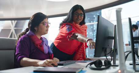 Two Diverse Colleagues Having a Conversation While Busy Working on a Corporate Team Project. South Asian Female Designer Talking with an Indian Project Manager. Teamwork in a Business Startup - obrazy, fototapety, plakaty