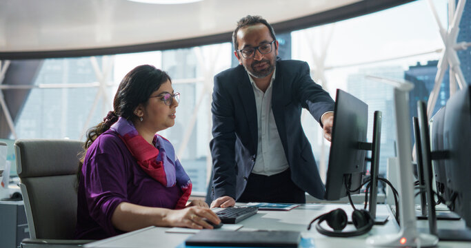 Financial Analyst Having a Meeting to Discuss a Business Project with a Handsome Indian Team Leader. South Asians Colleagues Using Desktop Computer, Comparing Reports and Data in a Modern Office
