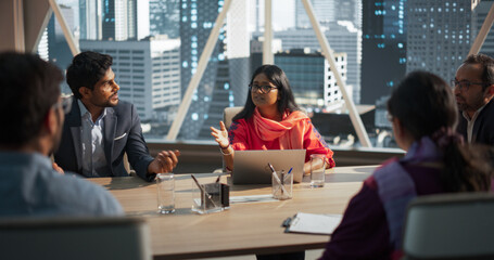 Indian Female Project Manager Makes a Business Presentation for a Diverse Creative Team in a Meeting Room in an Agency. South Asian Colleagues Gathered Around a Conference Table, Talking.
