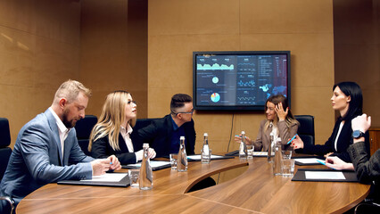 A diverse multinational team of professional business people meet in the conference room of a modern office. Creative team at the table discussing data analysis and planning a marketing campaign