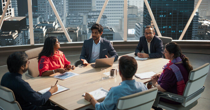 High Angle Footage of a Diverse Team of Professional South Asian Businesspeople Meeting in an Office Conference Room. Creative Team Sitting Behind a Table, Discussing Social Media Marketing Strategy - Powered by Adobe