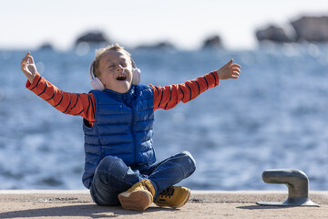 Happy boy with arms outstretched , sitting on a pier listening to music with headphones