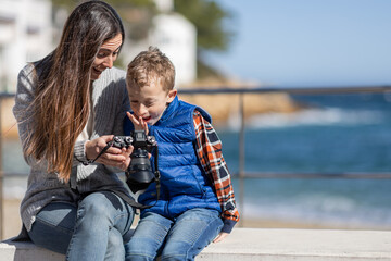 Little boy sitting next to his mother, showing surprise when reviewing photos on a camera, next to...