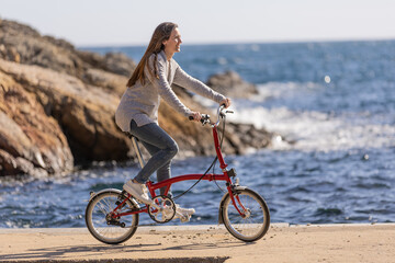 Side view of young woman riding an urban bicycle by the sea.