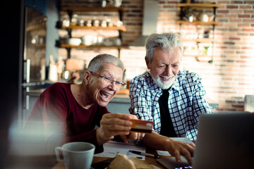 Smiling senior couple using credit card on laptop at home