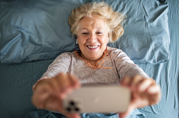 Senior woman lying in bed using smartphone