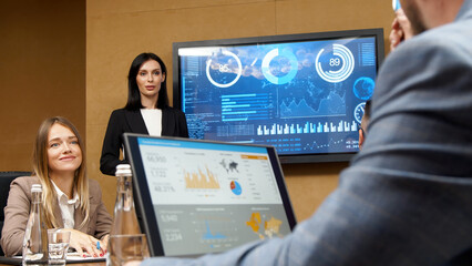 Business meeting in the conference room. A businesswoman is talking to her colleagues while an animated chart data is displayed on the computer screen.