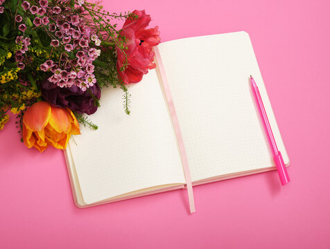 Colorful tulips lie on empty page of notebook, pink background. Space for your text.