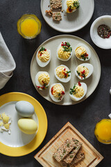 Happy Easter food background. Deviled eggs, orange juice, healthy crackers, dyed eggs on dark gray background with sunligh and harsh shadows, directly above - 753147103