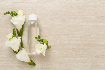 Obraz na płótnie Canvas Cosmetic bottle with freesia flowers on wooden background, top view