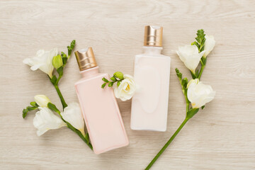 Cosmetic bottles with freesia flowers on wooden background, top view