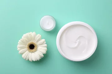 Tuinposter Moisturizing cream in open jars and gerbera flower on turquoise background, flat lay. Body care products © New Africa