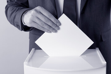 Man putting his vote into ballot box on background, closeup. Color toned