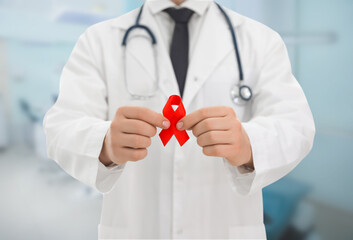 Cancer awareness. Doctor holding red ribbon on blurred background, closeup