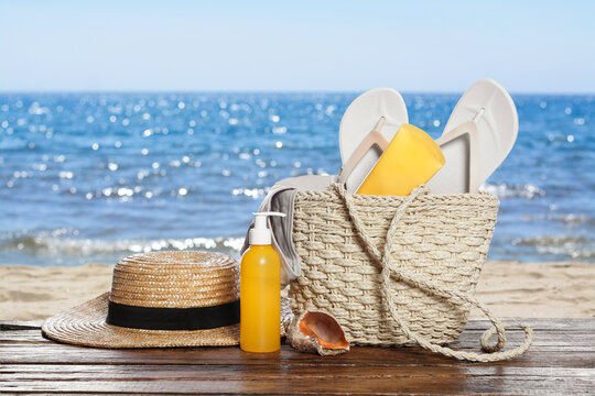 Stylish bag and other beach accessories on wooden table near sea