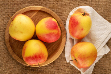 Several ripe sweet apples with wooden tray on jute cloth, macro, top view.