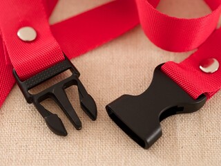 Two ends of a black contoured side release plastic buckle with red nylon belt on a beige textile background