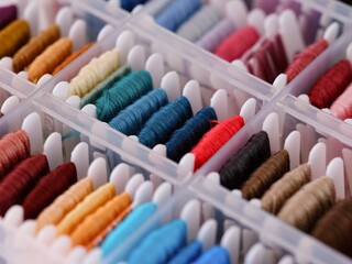 Bobbins with different colour embroidery threads in a plastic sorting box. Close-up