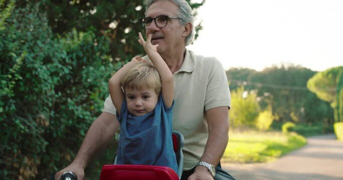 At sunset, a young grandfather takes his grandson on his bike along a road surrounded by nature and they have fun together