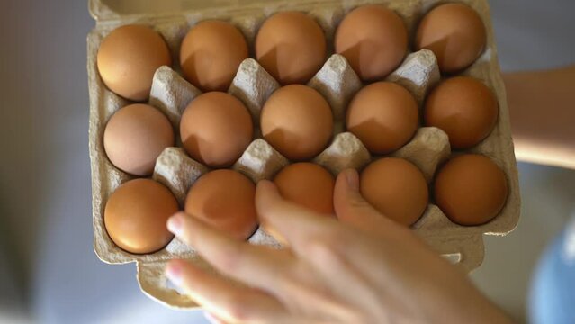 A hand holds a box of eggs. Fresh eggs in a box. Taking the egg out of the box. Choosing eggs for cooking. Eggs as an Easter attribute. Preparing for Easter.
