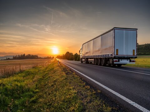 White truck driving on the asphalt road in rural landscape at sunset
