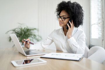 Professional woman multitasking with a phone call and computer work in a well-lit office space.