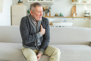 Fototapeta premium Pain on heart, heart attack. Unhappy middle aged senior man suffering from chest pain heart attack problems with health at home. Mature old senior grandfather touching chest experiencing infarction