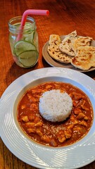 Indian Curry Meal with Naan and Refreshing Drink on Wooden Table
