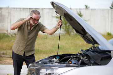 elderly man checking and try to fixing a broken car on the road